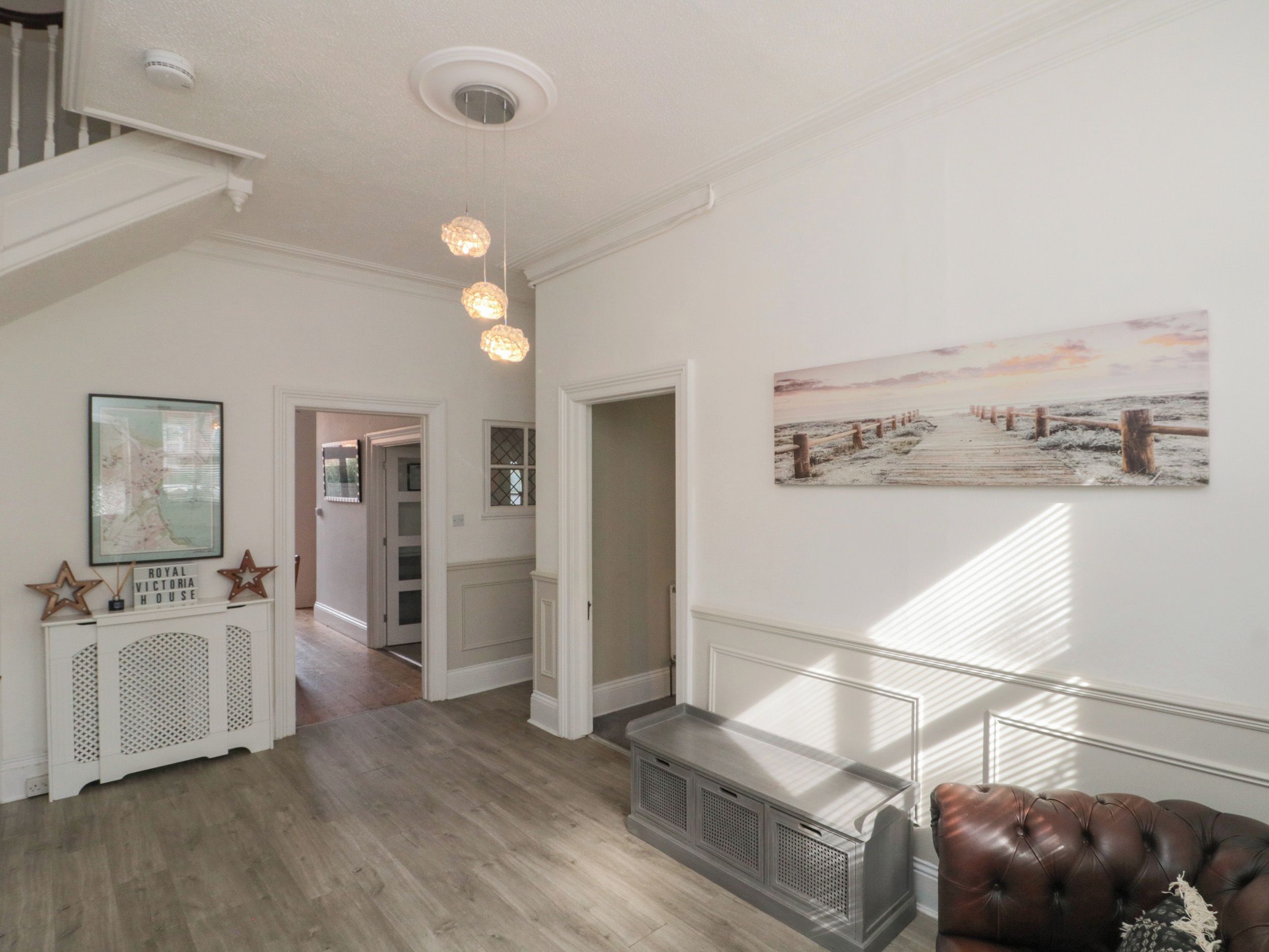 A spacious hallway with a wooden floor, a leather sofa, a fireplace, and a painting on the wall.