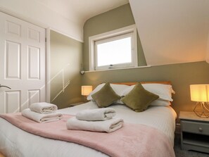 A neatly made bed with pillows and folded towels, a bedside lamp, and a window with blinds. - Royal Victoria House (Scarborough)
