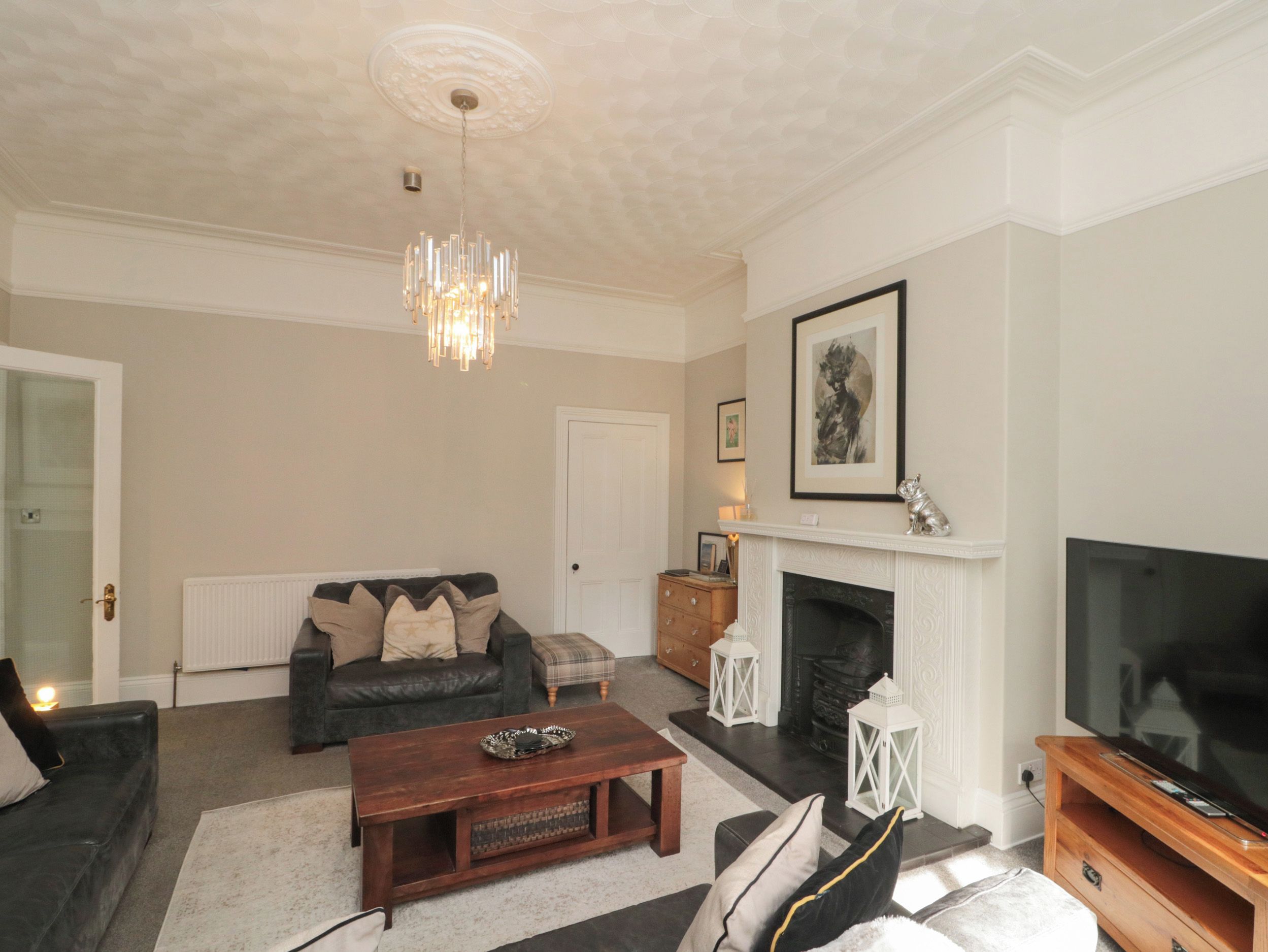 A living room with a fireplace, a television, and a chandelier.