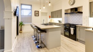 A modern kitchen with a central island, bar stools, a stove, and a clock on the wall. - Royal Victoria House (Scarborough)