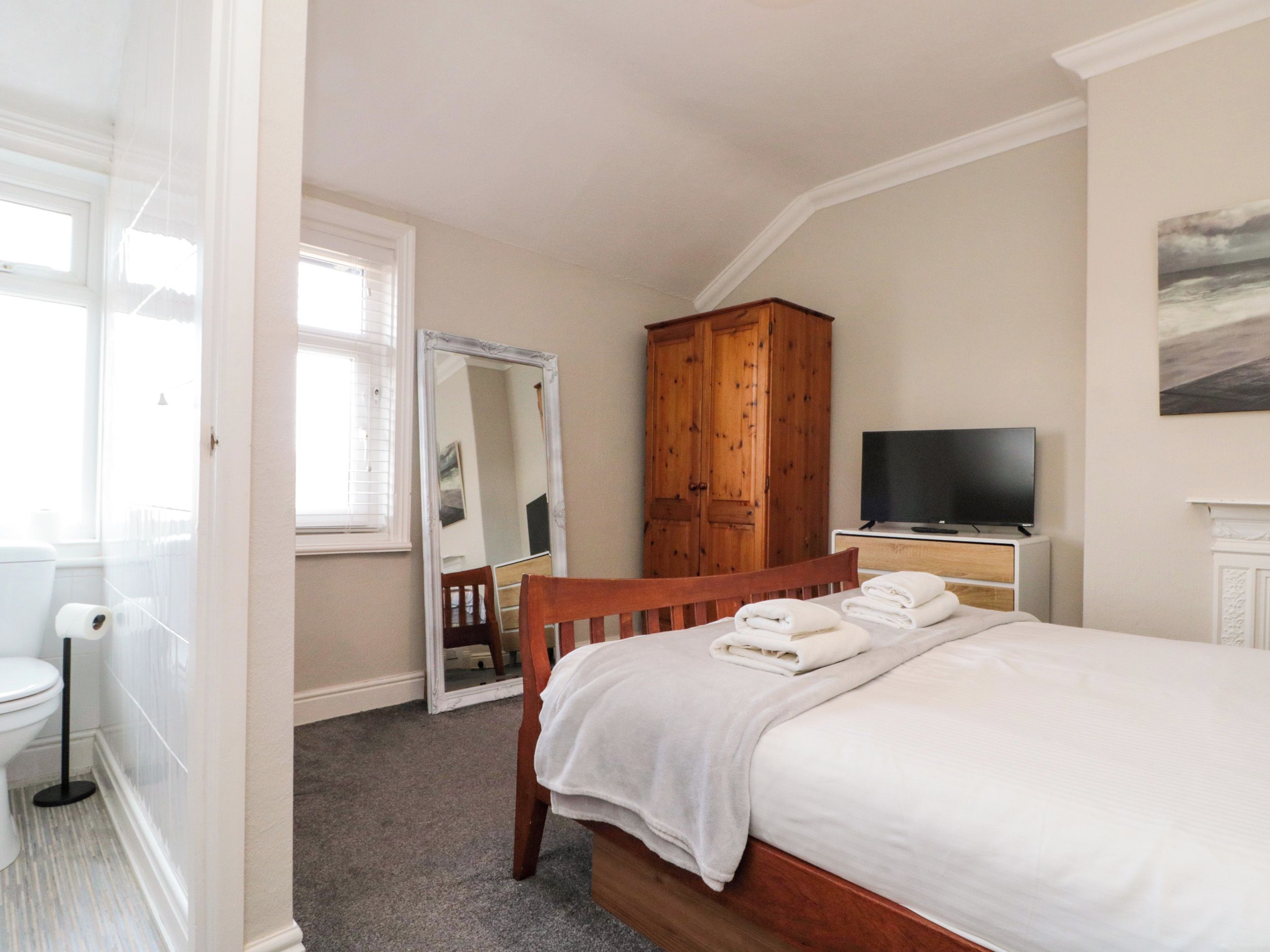 Quarto com cama, guarda-roupa de madeira, televisão e espelho.