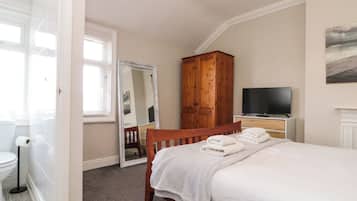 Quarto com cama, guarda-roupa de madeira, televisão e espelho.