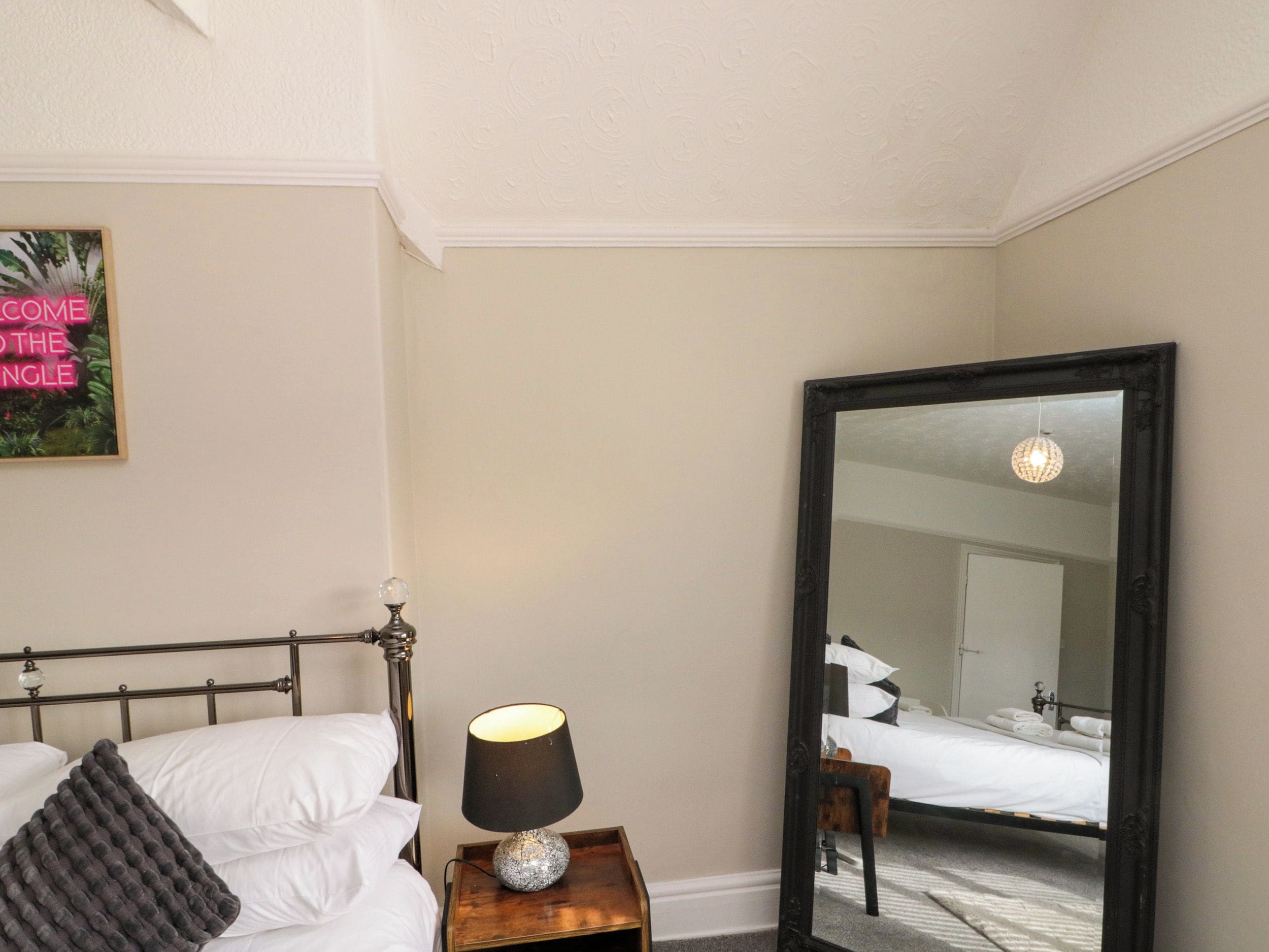 Una habitación de hotel con una cama, una lámpara de noche, un espejo y un cuadro colgado en la pared.