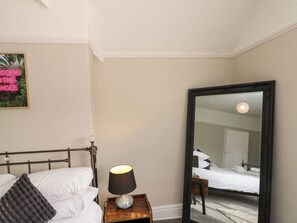 A hotel room with a bed, a bedside lamp, a mirror, and a wall-mounted picture. - Royal Victoria House (Scarborough)