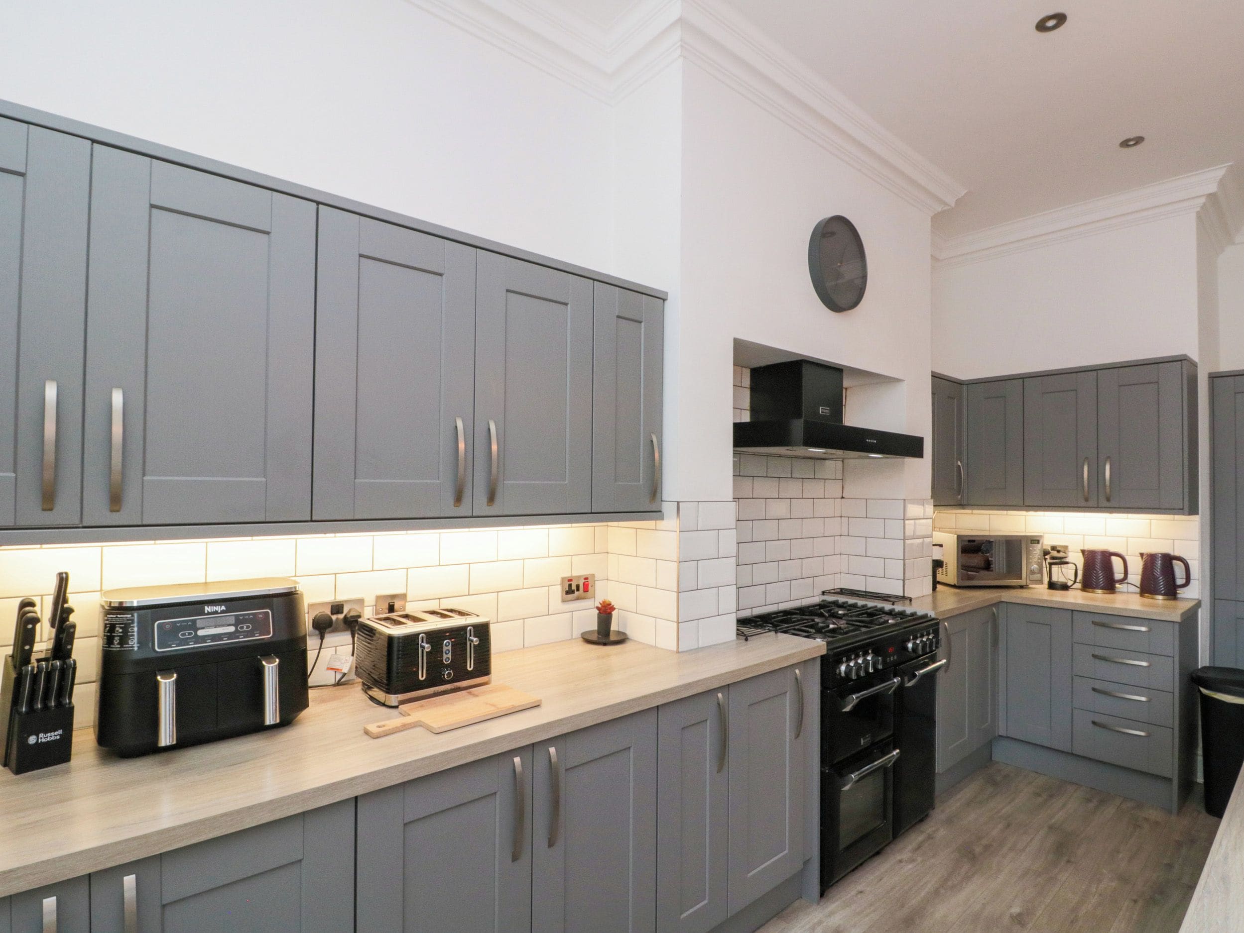 A modern kitchen with grey cabinets, a built-in microwave, a stove, and a toaster.