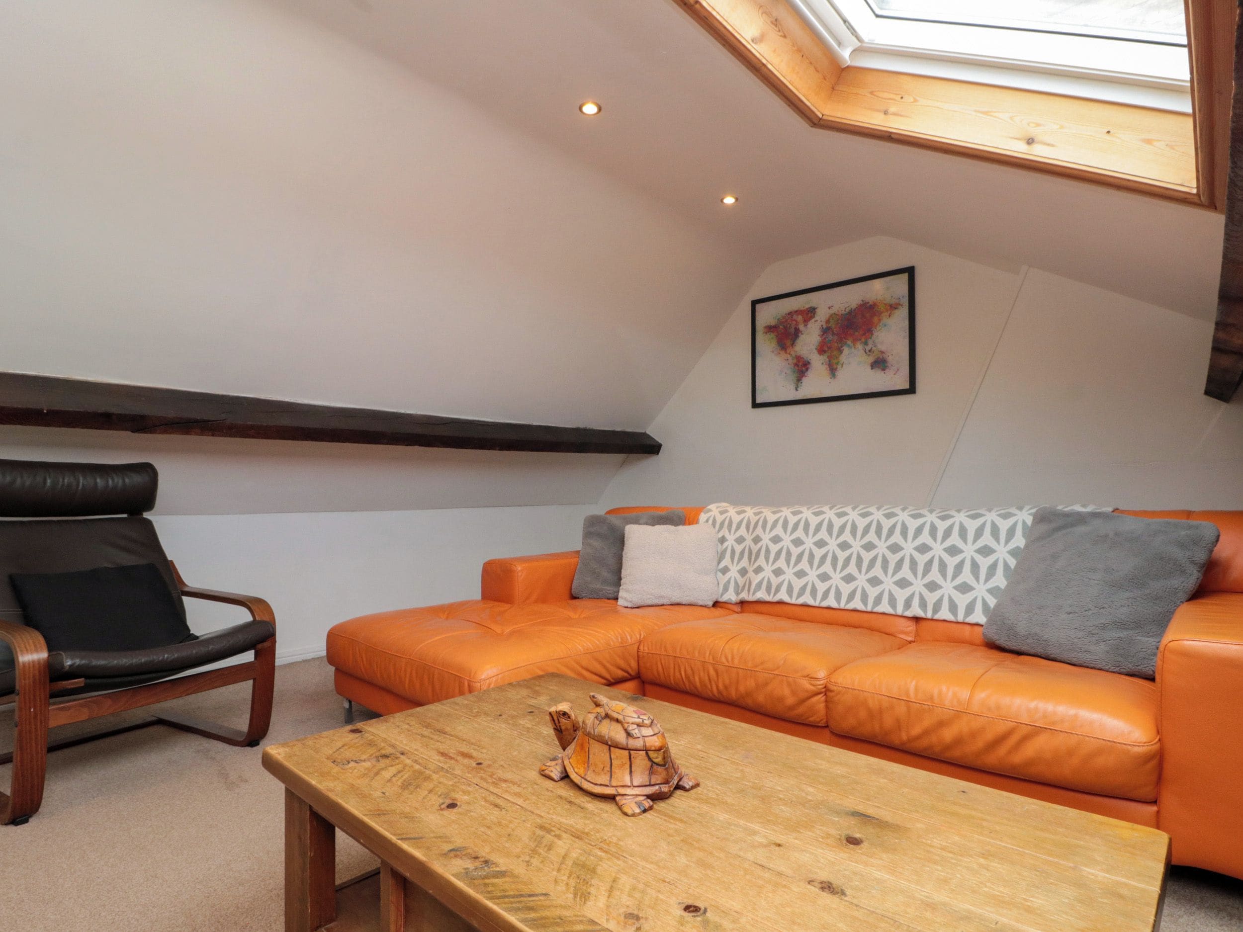 Un dormitorio tipo loft con techo inclinado, una mesa de madera, un sofá de cuero, un sillón de cuero y una obra de arte con un mapa del mundo.