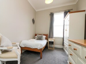 A bedroom with a bed, a chair, a dresser, and a window with curtains. - Royal Victoria House (Scarborough)
