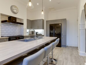 Een moderne keuken met een centraal eiland, roestvrijstalen apparatuur en hangende lampen.