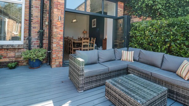 A modern outdoor living area with a built-in sofa and a coffee table, a brick wall, and a glass door leading to an interior space. - Royal Victoria House (Scarborough)