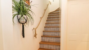 A wooden staircase with patterned tiles, a rope handrail, and a hanging plant. - West Cliff Apartment (Whitby)