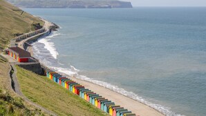 A coastal road with colorful beach huts along the seaside. - West Cliff Apartment (Whitby)