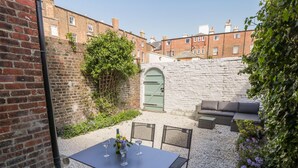 A patio with a table and chairs, a green door, and a stone wall. - West Cliff Apartment (Whitby)