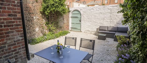 A patio with a table and chairs, a green door, and a stone wall.