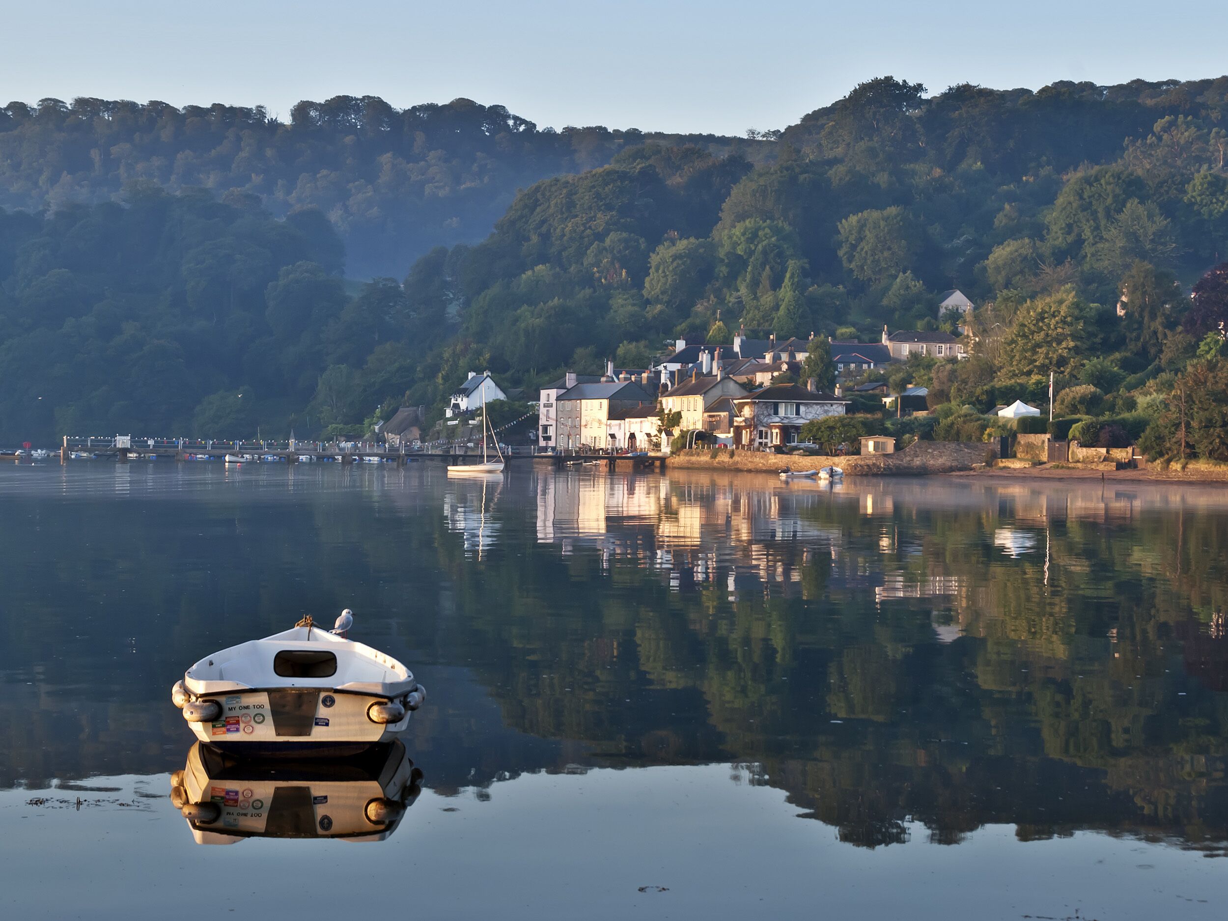 A calm lake with a boat in the foreground and houses on the opposite shore.