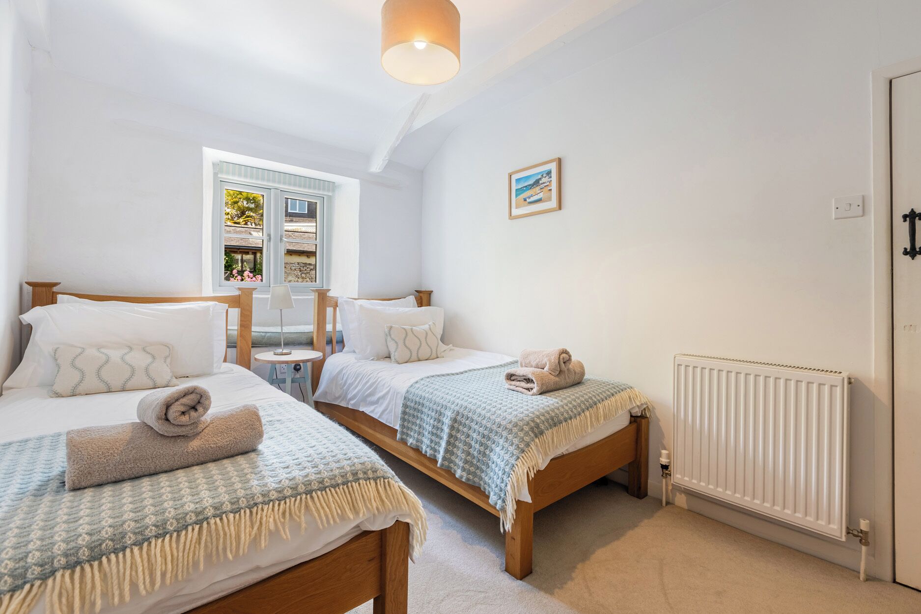 A bedroom with two beds, a window, a radiator, and a door.