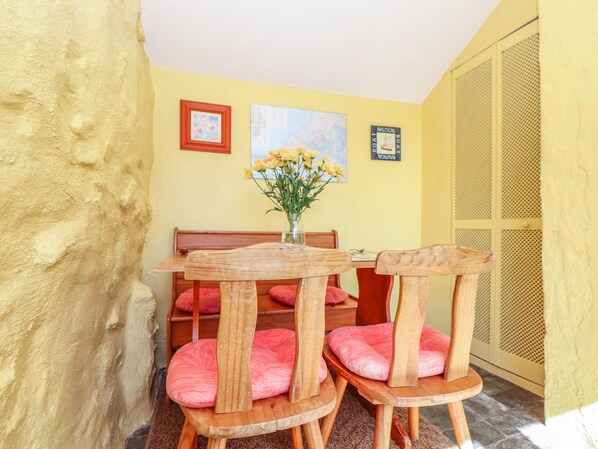 Un pequeño comedor con una mesa y sillas de madera, un jarrón de flores y una pared amarilla decorada con motivos náuticos.