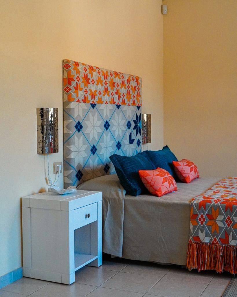 A bedroom with a patterned headboard, a bedside table with a lamp, and a bed with pillows.
