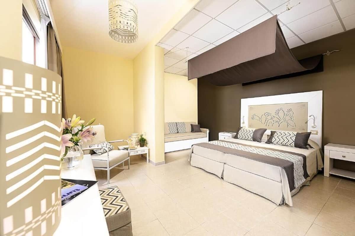 Una habitación de hotel moderna con una cama grande, un sofá, un escritorio y un ventanal amplio.