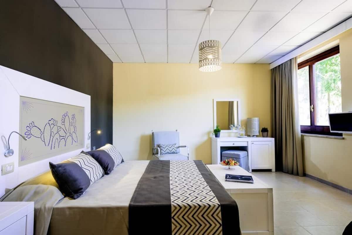 Una habitación de hotel con cama, escritorio, silla, televisión y una obra de arte en la pared.