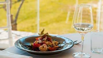 Ein Esstisch mit einem Teller Essen und einem Glas Weißwein vor einer Wiese und einem Gebäude.