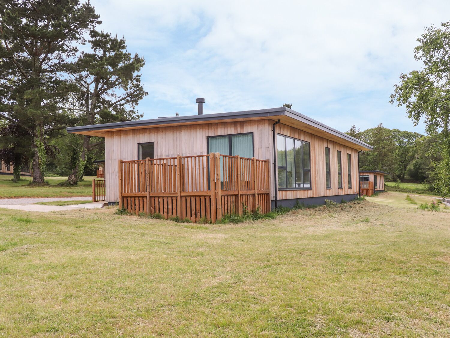 A modern wooden cabin with large windows, a deck, and a chimney.