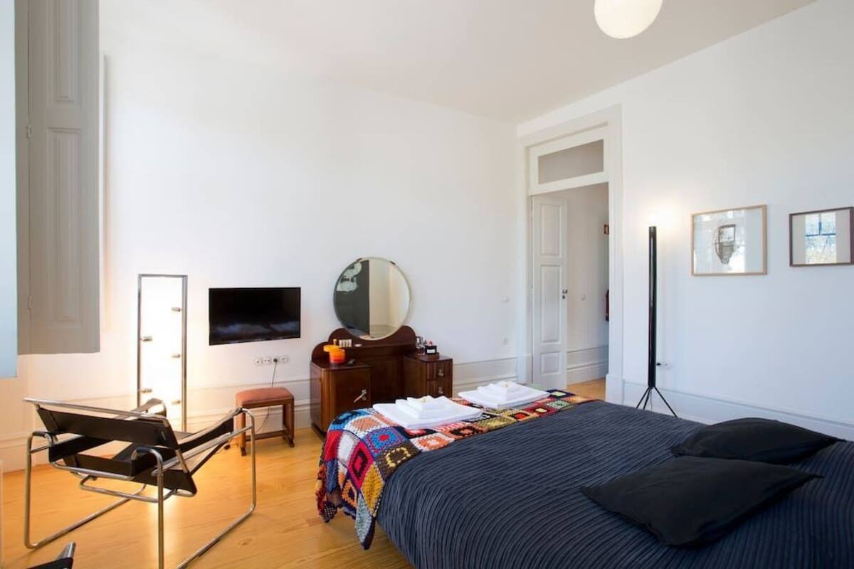 Une chambre moderne avec un lit, un bureau, une chaise, une télévision, un miroir et des tableaux encadrés accrochés au mur.