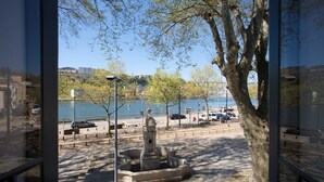 A view from inside a building looking out to a waterfront area with a statue, trees, and a clear sky. - 14 Esquadra  Cais das Pedras Guest House (Porto)