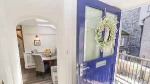 A blue door with a glass panel and a floral wreath, leading to a dining area with a wooden table, chairs, and a vase of sunflowers. - The Landings (Carnforth)
