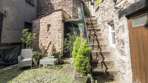 A narrow stone courtyard with a staircase leading to a second floor. There are potted plants and a wicker chair outside. - The Landings (Carnforth)
