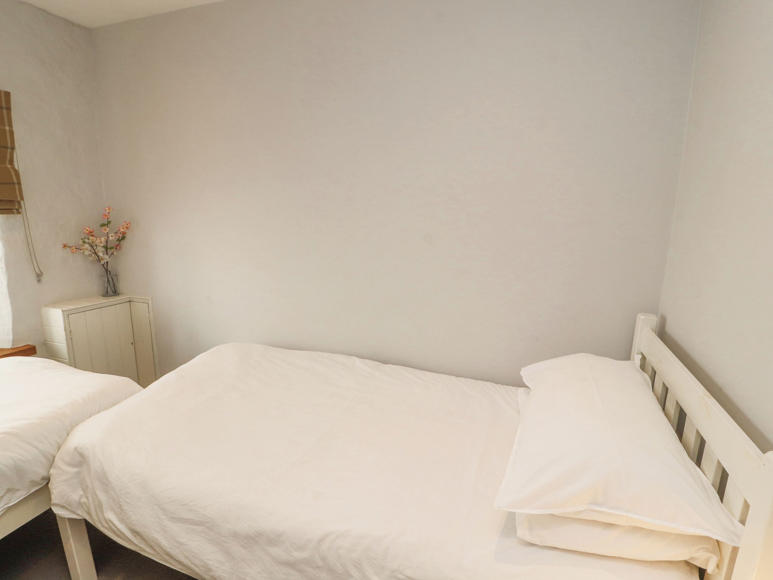 A simple, clean room with two single beds, a small bedside table, and a wall-mounted radiator.