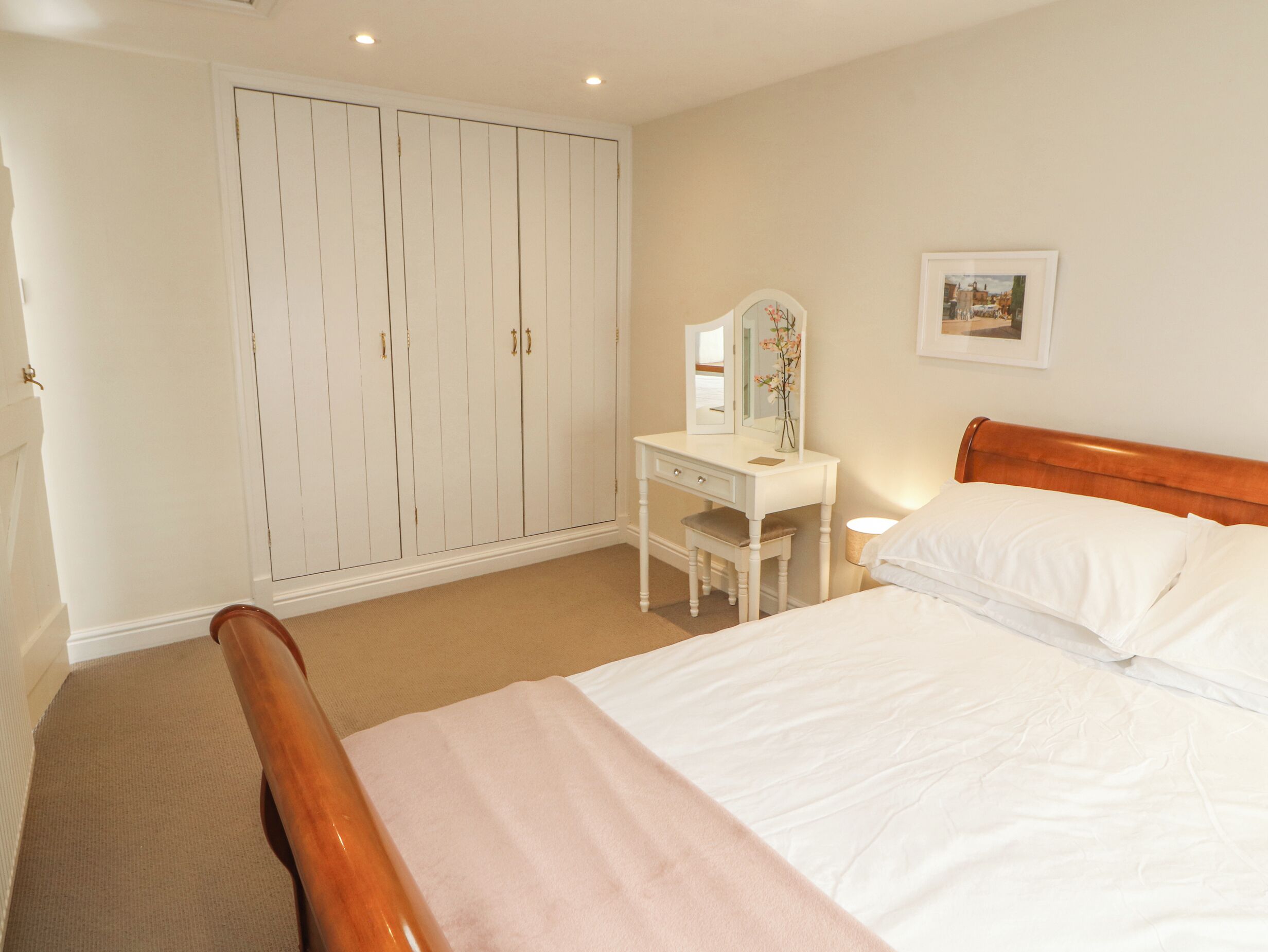 A bedroom with a bed, a white dresser, a mirror, and a wardrobe.