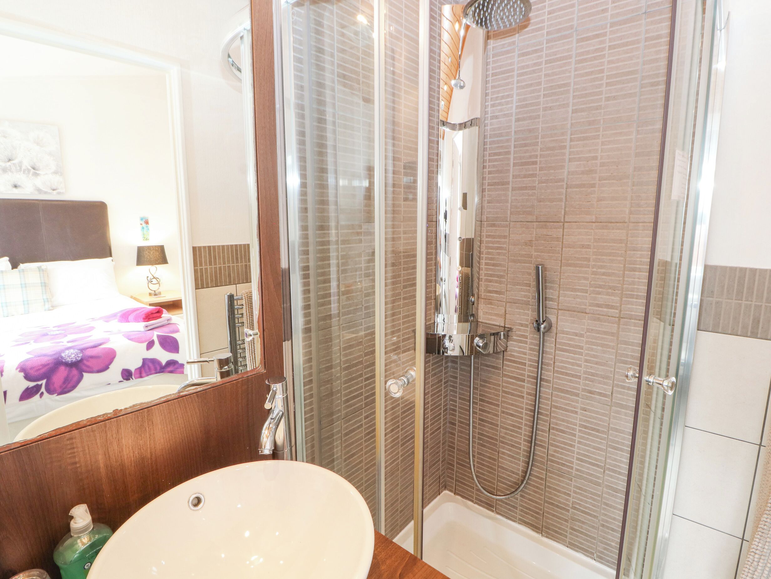 A modern bathroom with a glass-enclosed shower, a large mirror, and a wooden vanity with a sink.