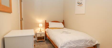 A bedroom with a wooden bed, a nightstand with a lamp, a white dresser, and a framed picture on the wall.