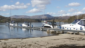 A marina with boats docked, calm water, and a mountainous backdrop.
