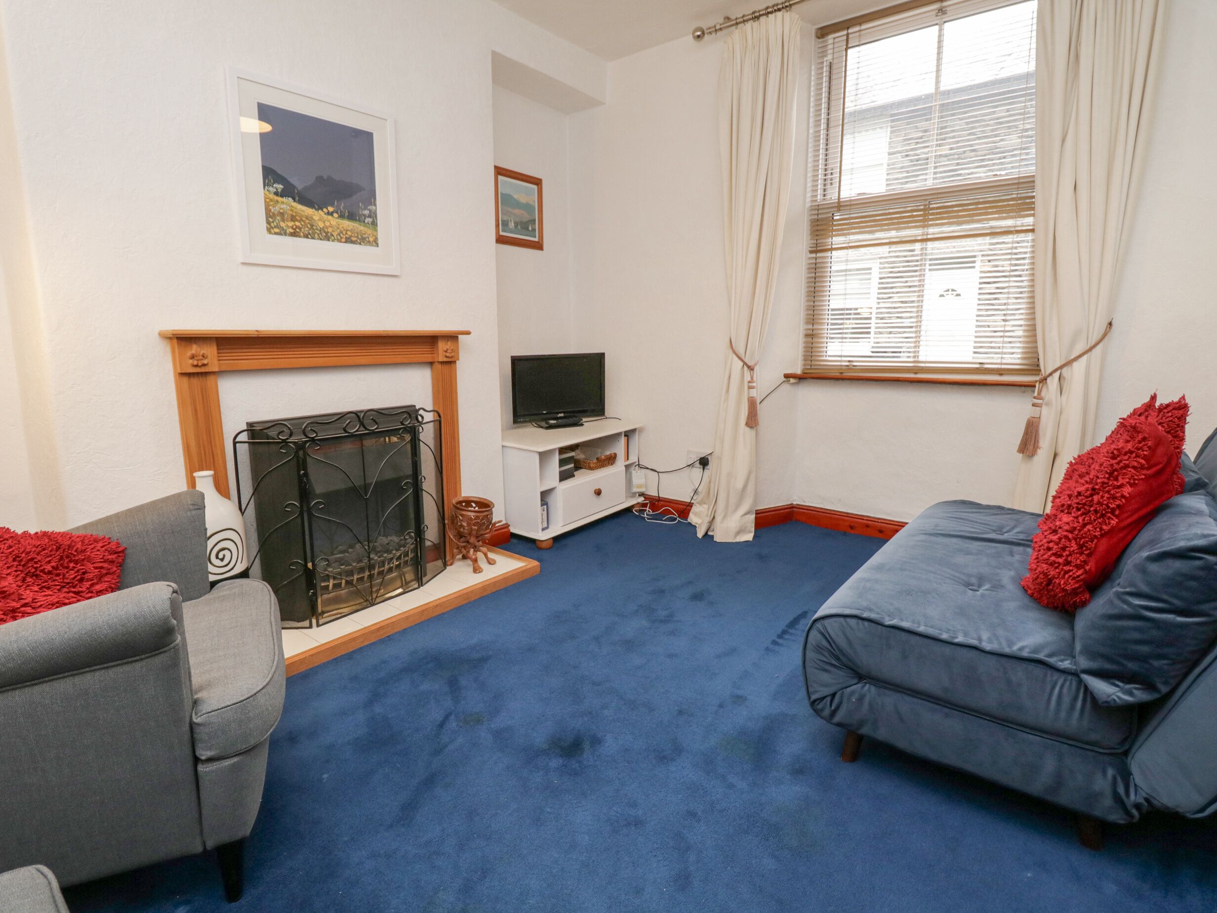 A living room with a fireplace, a sofa, a television, and a window with curtains.