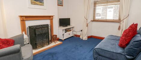A living room with a fireplace, a sofa, a television, and a window with curtains.