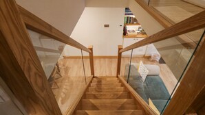 A wooden staircase with glass railings leading to a living area with a sofa and a bookshelf.