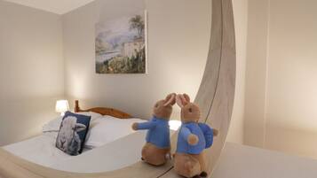 Una cama con cabecera de madera, un cuadro de un paisaje y dos peluches sobre la cama.