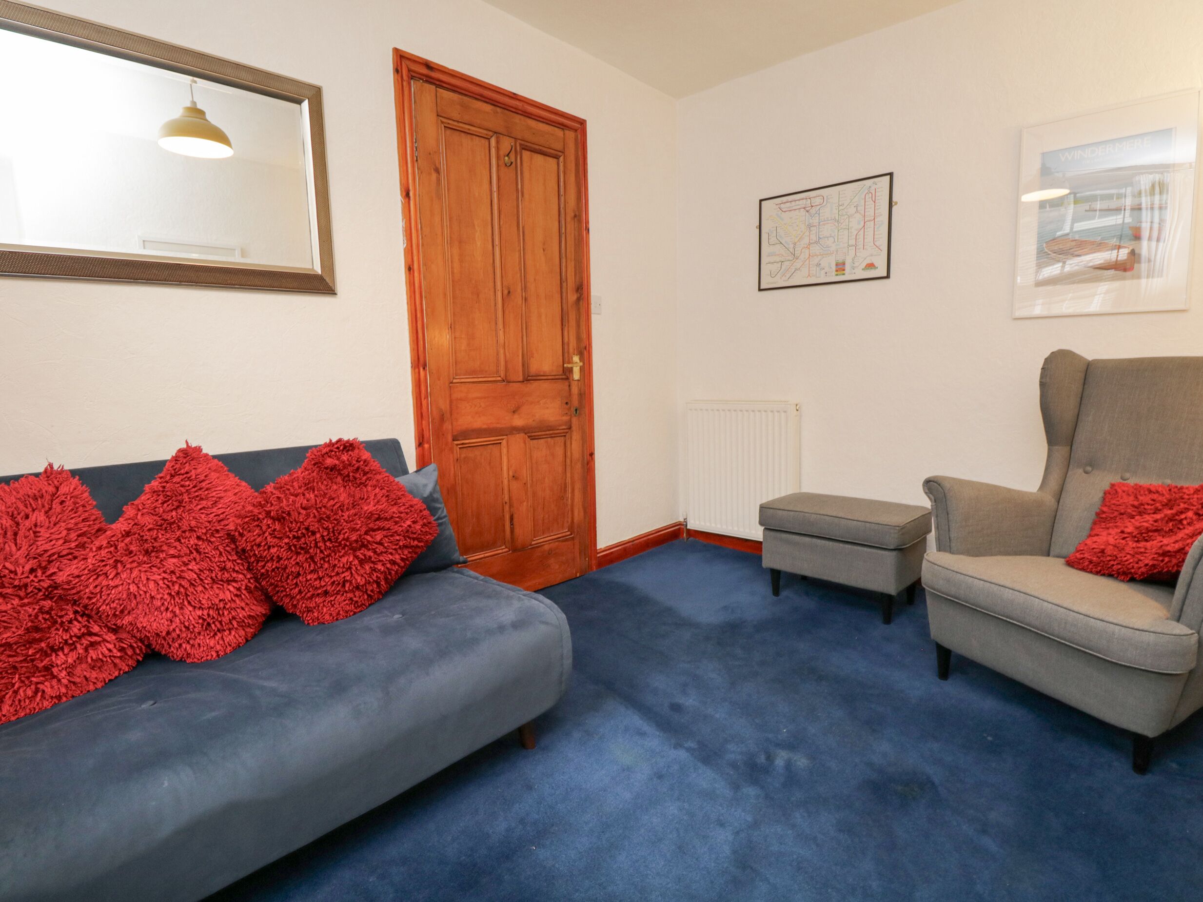 Een woonkamer met een blauwe bank, een grijze fauteuil en rode kussens.