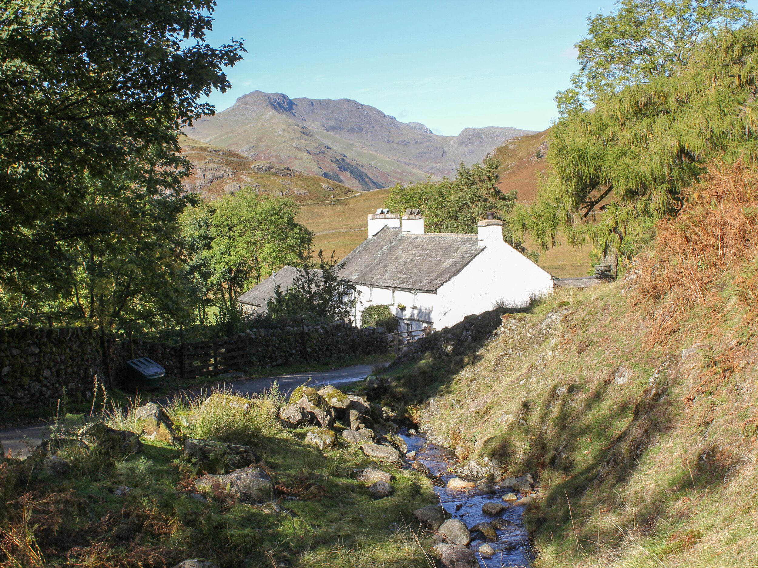 A white house with a stone wall and a stream running through a rural landscape.