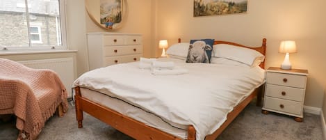 A bedroom with a wooden bed, white bedding, a bedside table with a lamp, a dresser, a mirror, and a painting on the wall.