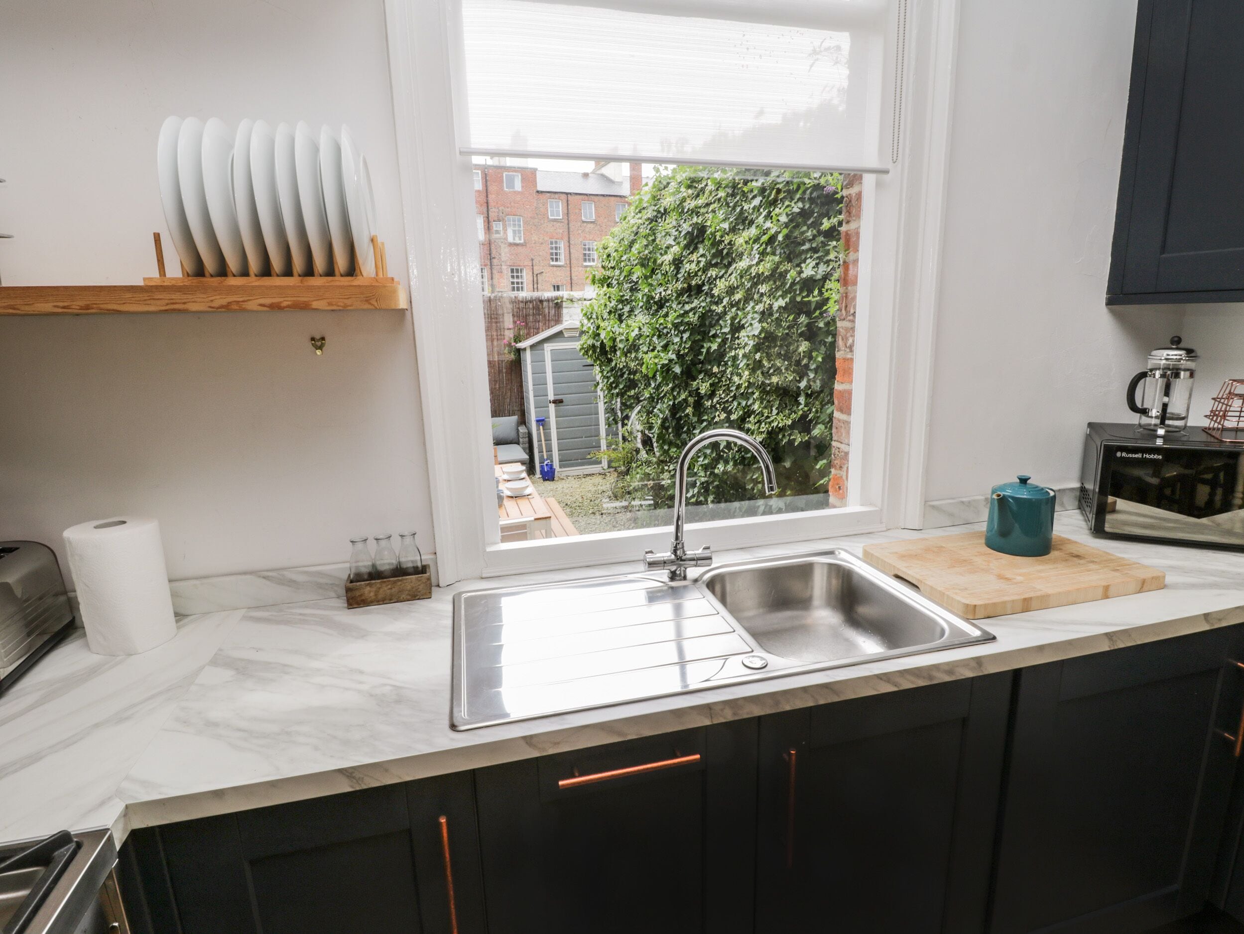 A modern kitchen with a stainless steel sink, wooden countertop, and dark cabinets.