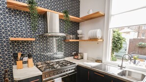 A modern kitchen with a gas stove, black cabinets, and a herringbone tile backsplash. - West Cliff House (Whitby)
