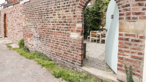 A brick wall with a small archway leading to a garden area with a table and chairs. - West Cliff House (Whitby)