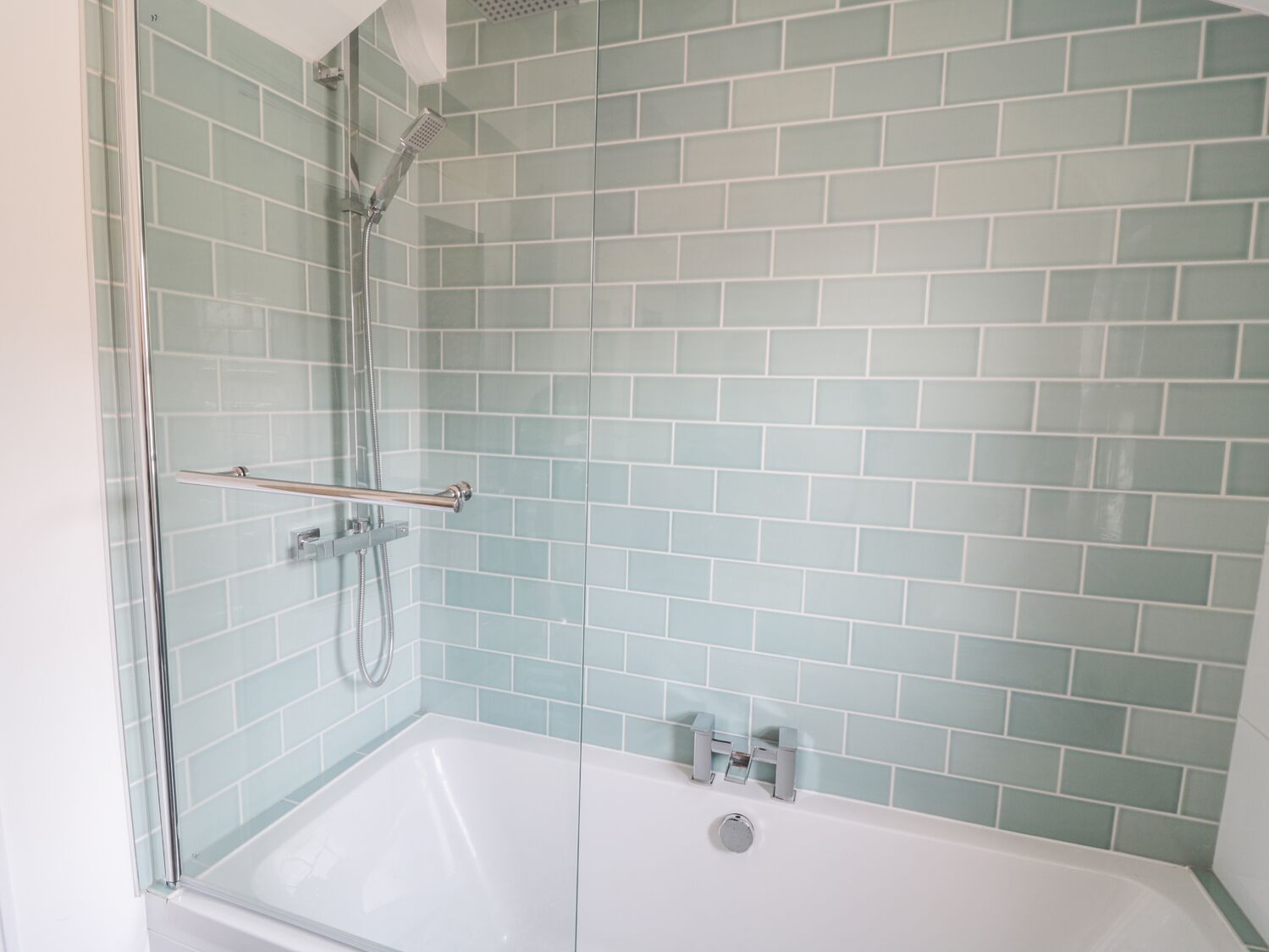 Une salle de bain avec une douche à parois de verre, une baignoire blanche et des murs recouverts de carreaux bleu clair.