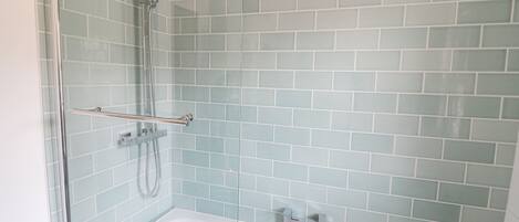 Une salle de bain avec une douche à parois de verre, une baignoire blanche et des murs recouverts de carreaux bleu clair.