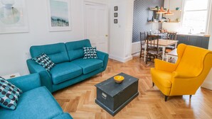 A modern living room with a teal sofa, a yellow armchair, and a black coffee table. - West Cliff House (Whitby)