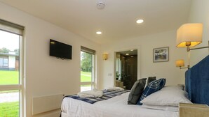 Une chambre à coucher comprenant un lit, un téléviseur fixé au mur, une fenêtre et une porte donnant sur une salle de bain.