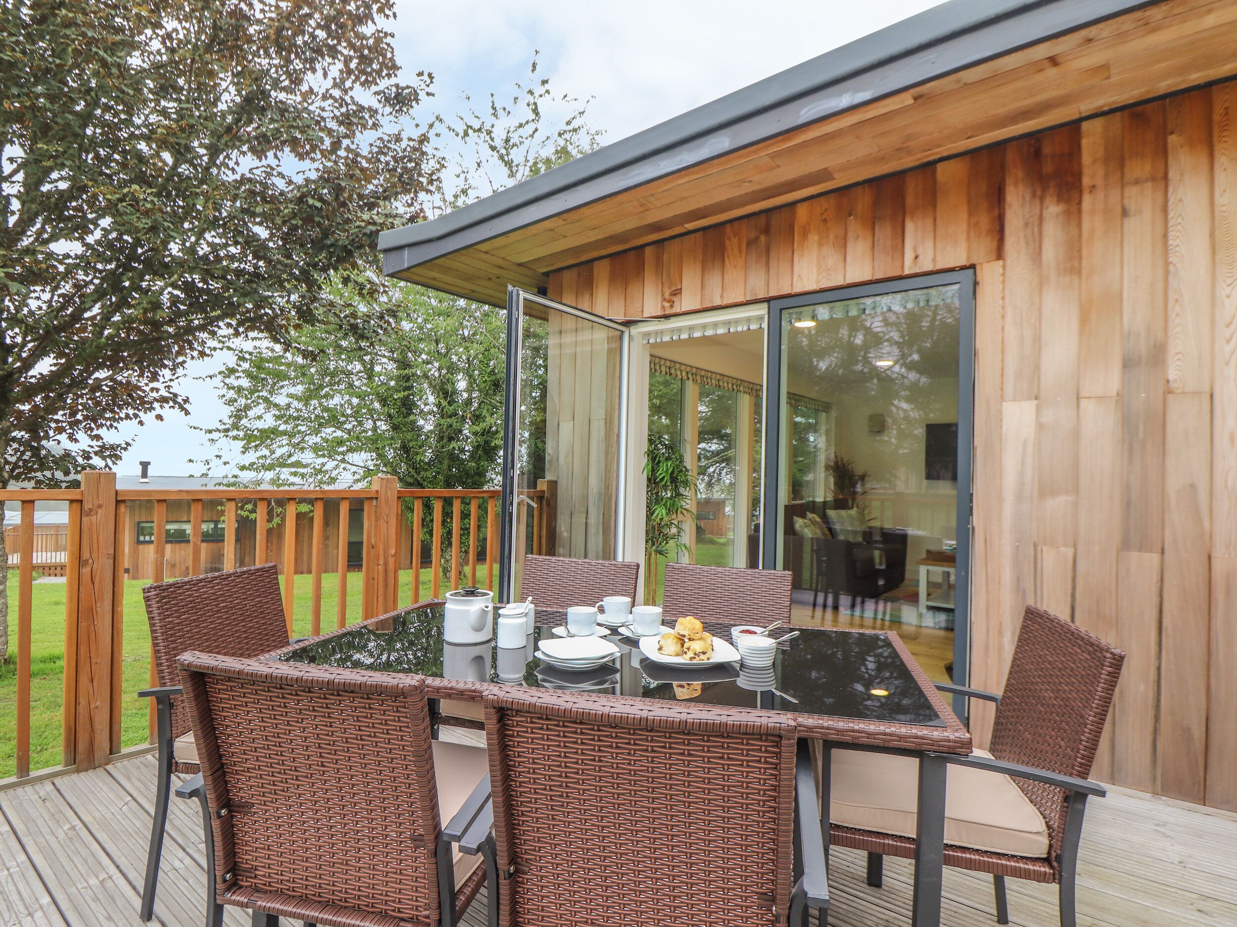 A deck with a glass-top table, wicker chairs, and a dining set.