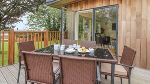 Une terrasse dotée d’une table à plateau en verre, de chaises en osier et d’un ensemble de mobilier de salle à manger.